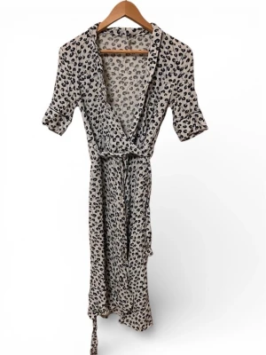 Vit och svart omlottklänning Ganni - Säljer en vit och svart omlottklänning från Ganni i storlek 34. Klänningen har leopardmönster, trekvartsärm och knytband i midjan. Tillverkad i ett mjukt och lätt material som känns skönt mot huden. Perfekt för dig som gillar trendiga detaljer och mönster.