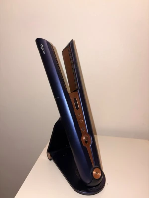 Trådlös dyson plattång - Trådlös dyson plattång som är marinblå och kopparfärgad (inte samma färg som på bilden från dysons hemsida, med samma modell). Den är använd ett fåtal gånger då jag har dubbletter, alltså är den i väldigt bra skick. Laddare tillkommer!💕💕 Köpt för 5 160 kr