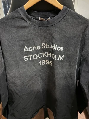 Svart långärmad t-shirt Acne Studios - Säljer en svart långärmad t-shirt från Acne Studios med tryck 'Acne Studios STOCKHOLM 1996' på bröstet. Tillverkad i 100% bomull och har en klassisk rund hals. Perfekt för dig som gillar stilrena och ikoniska plagg.