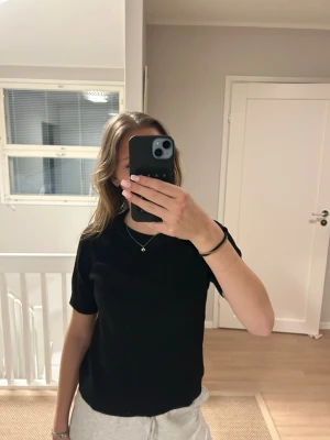 Svart ribbad stickad topp - Säljer en svart ribbad stickad topp med korta ärmar och rund hals. Toppen har en enkel och stilren design som passar perfekt till jeans eller kjol. Materialet är mjukt och ger en snygg struktur. Perfekt för dig som gillar en clean och klassisk look.