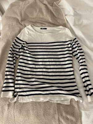Randig långärmad tröja Gina Tricot - Säljer en klassisk långärmad tröja från Gina Tricot i storlek XS. Tröjan är vit med marinblå horisontella ränder och har en rund halsringning. Materialet känns mjukt och lätt, perfekt för lager på lager under vår och höst.