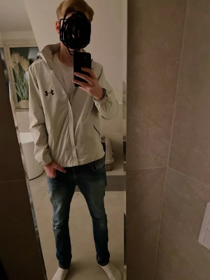 Windbreaker Under armour jacka  - En vit stilren jacka riktigt snygg. Luvan går och ta av och sätta på med dragkedja vilket är väldigt bra, va inte rädd att höra av dig om du har frågor!