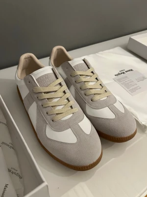 Maison Margiela sneakers  - Maison Margiela sneakers i vitt och beige med klassisk gummisula. Kan inget om dem, fick dem i present. aldrig använda. Kartong medföljer. Jag vet som sagt inget om dem och därför priset.