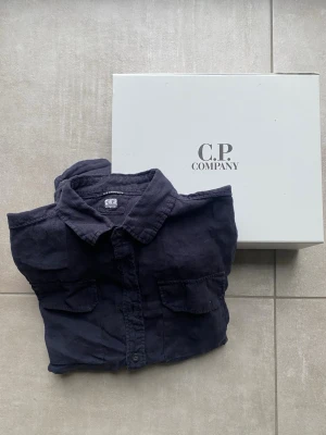 Marinblå linneskjorta från C.P. Company - Säljer en marinblå linneskjorta från C.P. Company med klassisk krage. Jag har använt den typ 1-2 gånger så den är helt ny.  Du får boxen med dig. De är XS men passar S. Priset är inte hugget i sten 