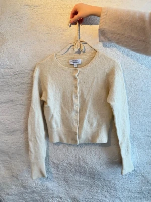 Vit kofta från & Other Stories - Superfin vit kofta från & Other Stories i mjuk ullmix. Croppad modell med rund halsringning och knappar framtill. Perfekt att slänga över en topp för en chill look. Långärmad och ribbade vid ärmslut och nederkant.