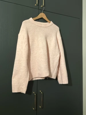Ljusrosa stickad tröja - Mysig ljusrosa stickad tröja med rund hals och ribbade muddar vid ärmslut och nederkant. Tröjan har en loose passform och är perfekt för kyliga dagar. Enkel och stilren design som är lätt att matcha. Använd några gånger men är fortfarande i bra skick!