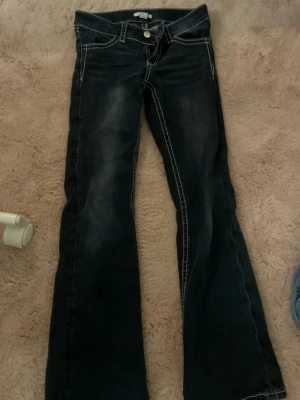 Mörkblå bootcut jeans Gina Tricot - Säljer ett par mörkblå jeans från Gina Tricot i storlek 152. Jeansen har bootcut-modell, låg midja och kontrastsömmar. Snygg broderad detalj på bakfickan och klassisk knappstängning framtill. 