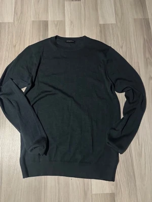 Svart stickad tröja från Bruuns Bazaar - En stilren svart stickad tröja från Bruuns Bazaar. Klassisk rund halsringning och långärmad modell i mjukt material. Perfekt till lager på lager och enkel att matcha med olika outfits.