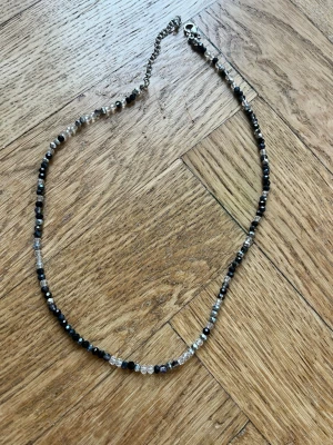 Halsband med pärlor  - Säljer ett halsband gjort i pärlor med svart, vit och grå. Halsbandet har en nostalgisk stil och passar perfekt för dig som gillar klassiska färger! 