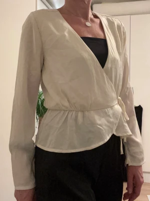 Snygg omlott topp i strl S - Omlott topp i ljus créme färg, lätt och tunt material. Knyter den så den är justerbar, passar s-m. Ny med prislapp kvar. Nypris 399 kr. 