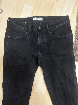 Svarta slim jeans Tom Tailor W33 L32 - Säljer ett par svarta slim fit jeans från Tom Tailor, modell Troy Slim. Jeansen har klassisk femficksdesign, svarta sömmar och bälteshällor. Materialet är jeans och passformen är smal utan att vara supertight. Perfekta till sneakers eller boots.