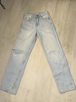 Ljusblå ripped jeans från Gina Tricot - Säljer ett par ljusblå jeans från Gina Tricot i modell 'perfect jeans'. De har raka ben, hög midja och slitna detaljer vid knäna Perfekta till sneakers eller boots.