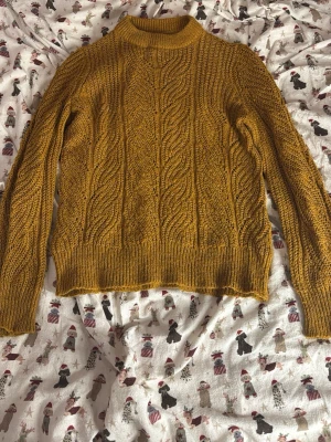 Senapsgul stickad tröja från Object - Stickad tröja i senapsgult från Object, storlek XS. Tröjan har ett snyggt flätmönster, ribbade muddar och hög hals. Perfekt för dig som vill ha en mysig och trendig look under kyliga dagar.