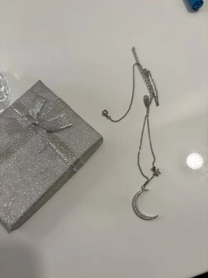 Äkta silver halsband med måne och stjärna - Äkta silver halsband i silverfärg med en glittrig måne och en liten stjärna som hänger i kedjan. Kedjan är tunn och smidig, perfekt för att ge en cool touch till din outfit. Kommer i en glittrig presentask. Är köpt från ur och Penn, orginalpris är 650kr. 