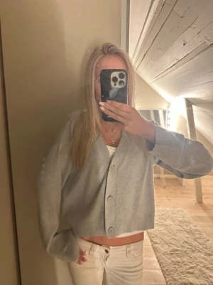 Ljusgrå kofta med stora knappar - Superfin ljusgrå kofta med oversized passform och stora knappar framtill. Koftan är croppad och har breda muddar vid ärmsluten. Perfekt att slänga över ett linne eller t-shirt för en chill look.