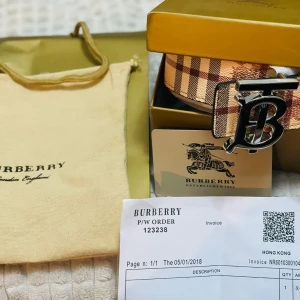 Burberry rutig bälte med silverdetalj - Säljer ett klassiskt rutig bälte från Burberry i beige, brunt och rött med en stor silvrig 'B'-logga som spänne. Bältet har den ikoniska Burberry-rutan och är tillverkat i skinn. Perfekt accessoar för att lyfta din outfit.