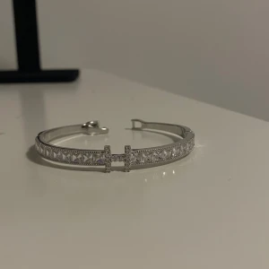 Armband i rostfritt stål  - Snyggt armband i silverfärg med glittrande stenar längs hela bandet och ett  H  i mitten.  Aldrig använt och rostfritt stål