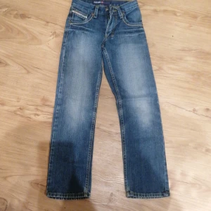 Buck Roger blå jeans med tryck - Snygga blå jeans från Buck Roger med coolt tryck på bakfickan och detaljerade sömmar. Klassisk femficksmodell med slitningar och kontrastsömmar. Märkespatch bak i midjan och logga på myntfickan. Perfekta för dig som gillar streetstyle.
