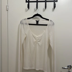 Vit ribbad långärmad topp Lindex - Säljer en vit ribbad långärmad topp från Lindex i storlek M. Toppen har v-ringning med snygg rynkdetalj framtill och är tillverkad i ett mjukt, stretchigt material. Perfekt att styla med jeans eller kjol för en clean look. Säljer likadan topp i grönt.