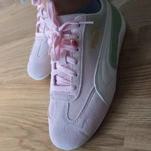 Puma speedcat strawberry matcha - Säljer ett par snygga pastellrosa sneakers från Puma med ljusgröna detaljer på sidan och guldfärgad logga. Skorna har snörning och en liten jordgubbsberlock på ena skon. Ovandelen är i mocka och de har en klassisk rund tå.