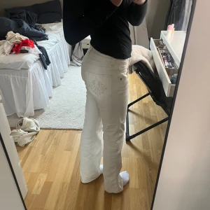Vita bootcut jeans med broderad ficka - Snygga vita jeans med bootcut passform och låg midja. Jeansen har broderad detalj på bakfickan och dubbla knappar framtill. Sitter bekvämt och ger en clean look.