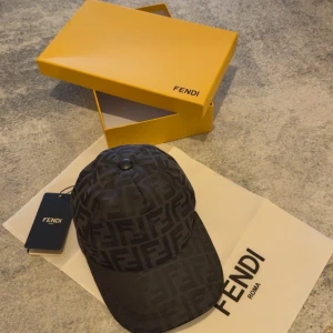 Svart Fendi keps med FF-mönster - Snygg svart keps från Fendi med det ikoniska FF-logomönstret över hela kepsen. Justerbar rem baktill i skinn med Fendi-gravyr. Kepsen har böjd skärm och klassisk form, perfekt för dig som vill ha en exklusiv streetstyle-look.