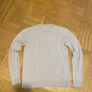 Beige stickad tröja Jack & Jones XS - En stilren beige stickad tröja från Jack & Jones i storlek XS. Tröjan har rund halsringning, långa ärmar och ribbade muddar vid ärmslut och nederkant. Perfekt för lager-på-lager och enkel att matcha med jeans eller chinos.