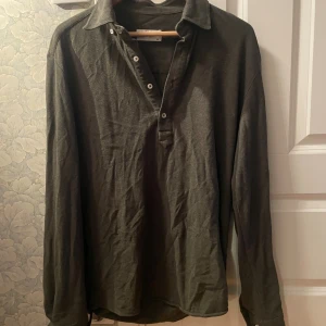 Mörkgrön henley från John Henric - Snygg mörkgrön henley-skjorta från John Henric i storlek M. Skjortan har klassisk krage, långa ärmar och flera vita knappar framtill. Materialet är mjukt och känns som bomull, perfekt för en chill och stilren look.