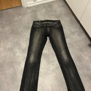 Svarta jeans från Lee - Säljer ett par svarta  jeans från Lee med slitna detaljer och snyggt tvättad look. Jeansen har klassisk femficksdesign, låg midja och smal passform hela vägen ner.