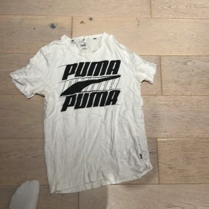 Vit Puma t-shirt med stor logga - Vit t-shirt från Puma i storlek S med fet svart Puma-logga tryckt på bröstet. Klassisk rund hals och korta ärmar. Materialet är mjuk bomull som känns skönt mot huden. Perfekt för dig som gillar sportiga och stilrena plagg med tydlig branding.