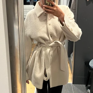 Vit Ullkappa Filippa K - Säljer en stilren beige ove från Filippa K med knappar framtill och ett matchande bälte i midjan. Jackan har klassisk krage, långa ärmar och är tillverkad i mjukt ullmaterial. Perfekt för dig som gillar minimalistisk och clean look. Storlek 36 nypris 4000kr
