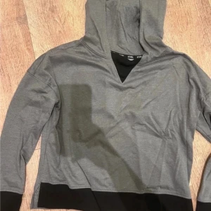 Grå hoodie med svart kant från Etnies - Snygg grå hoodie från Etnies med svart kant nedtill och vid ärmslut. Tröjan har en huva och en cool v-ringad detalj vid halsen. Perfekt för chill dagar och streetwear-stil. Långärmad och i mjukt material. Snabb leverans 📦 