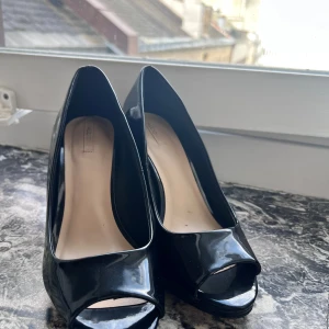 Svarta peep toe pumps från ALDO - Stilrena svarta pumps från ALDO i glansigt material med öppen tå och hög klack. Skorna har en klassisk siluett och plattformsula som ger extra höjd. Perfekta för dig som vill ha en elegant look med en modern twist.snabb leverans 📦✨kolla på mina andra plagg ( bästa priser)