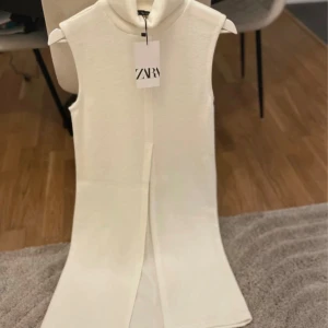 Vit ärmlös långklänning från Zara - Supersnygg vit långklänning/tunika från Zara med hög krage och ärmlös design. Klänningen har en rak siluett och en diskret slits framtill. 
