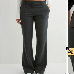 Grå kostymbyxor från Nelly, storlek 38 - Snygga grå kostymbyxor från Nelly i storlek 38. Byxorna har en rak och lite vidare passform med hög midja och klassiska detaljer som bälteshällor och knappstängning. Perfekta för en clean och stilren look. Aldrig använda prislapp sitter kvar