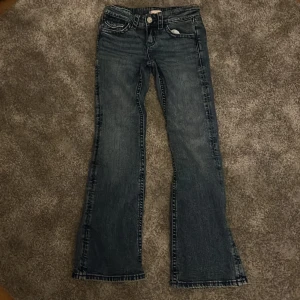 Blå bootcut jeans från Gina Tricot - Snygga blå bootcut jeans från Gina Tricot i storlek 152. Jeansen har klassisk femficksdesign, markerade sömmar och coola detaljer på bakfickorna. Perfekt för dig som gillar en lite utsvängd look och vill ha ett par jeans som sticker ut.