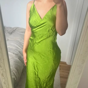 Grön långklänning från Zara 💚 - Säljer en snygg grön långklänning från Zara med omlott-v-ringning och tunna axelband. Klänningen har en figurnära passform och är gjord i ett glansigt, silkigt material som ger en lyxig känsla. Perfekt för dig som vill sticka ut med färg och stil 💚