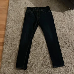 Mörkblå jeans från Kappahl  - Snygga mörkblå jeans Hampton Republic från Kappahl med klassisk femficksdesign och kontrastsömmar. Modellen har rak passform och är tillverkad i slitstarkt jeanstyg. Nytt skick på dem imed att de bara använts 1-2 gånger. Snygga jeans för övrigt som passar i vardagen. Hör av er om ni har frågor!