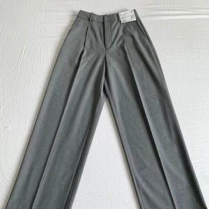 Grå vida kostymbyxor från Uniqlo XS - Snygga grå kostymbyxor från Uniqlo i storlek XS. Vida ben och hög midja ger en clean och modern look. Gjorda i en mix av återvunnen polyester, viskos och elastan för skön passform. Perfekta att styla med en crop top eller oversized hoodie.
