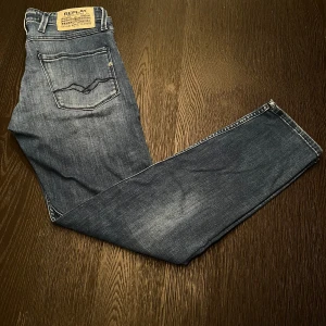 Replay Anbass slim fit jeans blå - Snygga blå Replay Anbass jeans i slim fit med klassisk femficksdesign och diskreta slitningar. Jeansen har normal midja och raka ben, tillverkade i mjukt bomullstyg med stretch för extra komfort. Perfekta för dig som gillar en stilren och modern look.