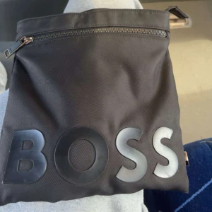 Svart axelväska från BOSS - svart boss väska stor på insidan har 3 fickor en utanför som ni ser på bilden o två på insidan inga hål eller något köpt för 1,200kr säljer för 500kr hör av dig av intresse