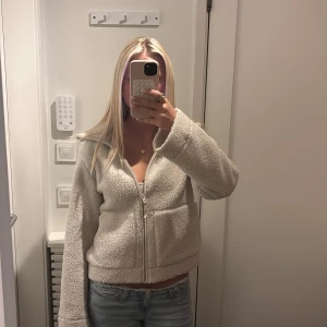 Beige teddyjacka med dragkedja - Mysig beige teddyjacka med krage och hel dragkedja framtill. Jackan har en loose passform och är tillverkad i fluffigt fleece-material som ger en chill vibe. Perfekt för att hålla sig varm och se snygg ut. Passar dig som gillar avslappnad stil.