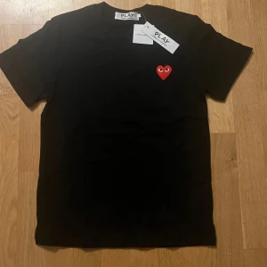 Svart Comme des Garçons Play t-shirt - Svart t-shirt från Comme des Garçons Play med det ikoniska röda hjärtat med ögon broderat på bröstet. Klassisk rund hals och korta ärmar. Tillverkad i mjuk 100% bomull för skön komfort. Perfekt för dig som gillar stilrena designer med en twist.