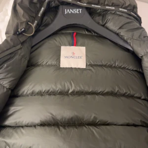 Olivgrön Moncler pufferjacka med huva - Säljer en äkta olivgrön pufferjacka från Moncler använd 1-2 gånger kommer med huva och dragkedja. Jackan har Moncler-logga på ärmen och quiltad nedre del, vilket ger en schysst streetstil. Materialet är syntet och dun, perfekt för kalla dagar. Snygg och funktionell design. Kan byta mot en jacka och kom med förslag gällande pris då.