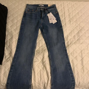 Bootcut jeans från Gina Tricot, blå - Bootcut jeans från Gina Tricot i klassisk blå tvätt med låg midja. Modellen har raka ben som blir vidare nedtill och snygga bakfickor. Perfekt jeansmaterial med skön stretch och cool passform. Snygga att matcha med sneakers eller boots.