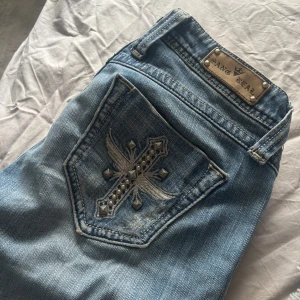 Blå bootcut jeans från Sang Real - Snygga blå jeans från Sang Real med bootcut passform. Jeansen har coola detaljer som metallknappar med logga, broderad bakficka med nitar och korsmotiv. Materialet är klassisk jeans och midjan är låg. Insydda vid midjan så de passar Xs men går att sprätta upp så att de passar S-M❤️Långa i benen, passar mig som är 172