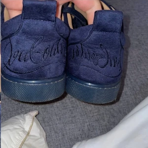 Mörkblå Christian Louboutin sneakers - Snygga mörkblå sneakers från Christian Louboutin i mocka med klassisk röd sula och signaturbroderi på hälen. Skorna har rund tå, platt sula och snörning framtill. Perfekt för dig som vill sticka ut med exklusiva detaljer och lyxig känsla. Det är A kopior och har tyvärr tappat bort boxen under flytten 