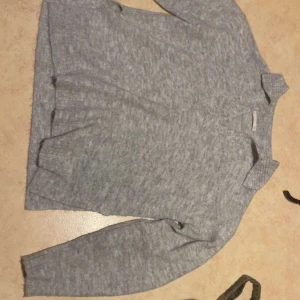 Grå stickad kofta med krage - Mysig grå stickad kofta med krage och v-ringning. Långärmad modell med ribbade muddar och en enkel, stilren look. Perfekt för lager-på-lager och passar till det mesta i garderoben.