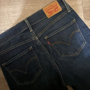 Levi's 314 shaping straight jeans blå - Snygga mörkblå Levi's 314 shaping straight jeans med klassiska fem fickor och gul kontrastsöm. Modellen har rak passform och normal midja, tillverkade i stretchigt denim för extra komfort. Perfekt för dig som gillar tidlös stil och vill ha jeans som sitter schysst hela dagen. Är även lite utsvängda 