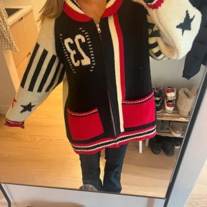 Jaded London  - Säljer en oversized stickad cardigan jacka med dragkedja, coola svarta och röda detaljer, stora röda fickor och mönster med stjärnor och ränder. 